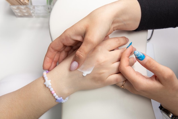Een manicure brengt handcrème aan op vrouwelijke handen na een hardwaremanicure in een schoonheidssalon