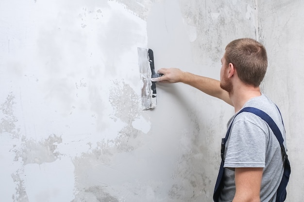 Foto een mannelijke arbeider verspreidt het stopverfmengsel en maakt de muur vlak.