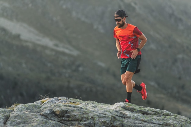 Een mannelijke atleet met een baard rent over rotsblokken in de bergen