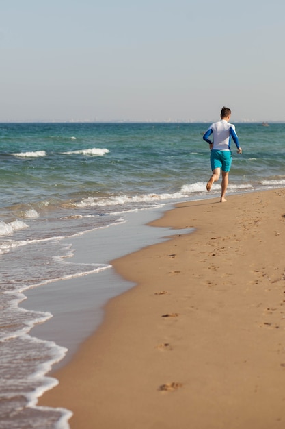 Een mannelijke atleet rent langs het strand in blauwe korte broek langs de zeekust van cyprus kopieerruimte