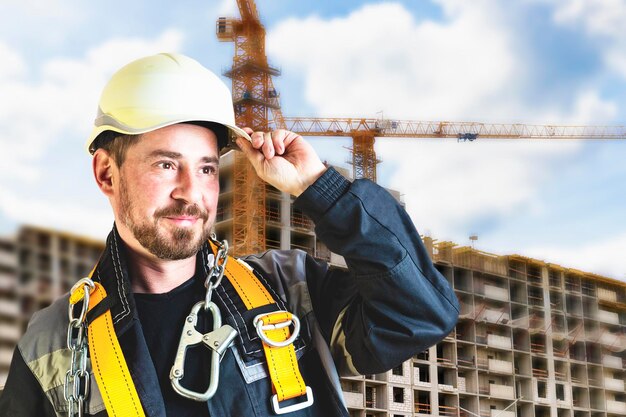 Een mannelijke bouwer met een witte helm tegen een wazige achtergrond van een bouwplaats met een blauwe lucht Positieve burgerlijk ingenieur met een baard