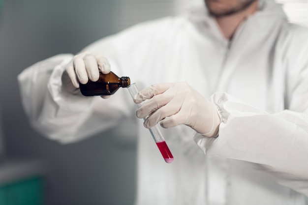 Een mannelijke chemicus houdt een glazen reageerbuis in zijn hand met wat roze vloeistof en giet er een nieuw reagens in.