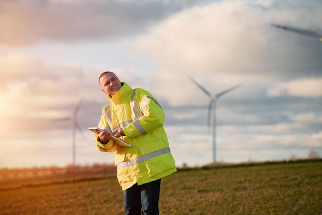 Een mannelijke ingenieur staat in een windturbineveld met een prachtige hemelachtergrond