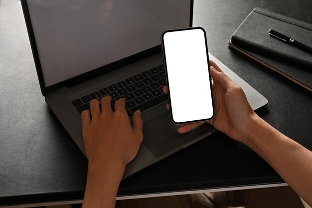 Een mannelijke kantoormedewerker of zakenman die een smartphone vasthoudt en typt op een notebooklaptop