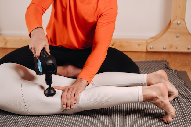 Een mannelijke masseur masseert het lichaam van een meisje met een percussiemassageapparaat om zich voor te bereiden op een stretchingsimulator