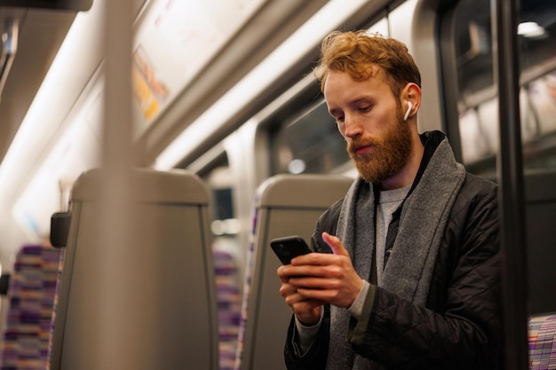 Een mannelijke metropassagier zit in een trein en luistert naar muziek op een koptelefoon en gebruikt een smartphone