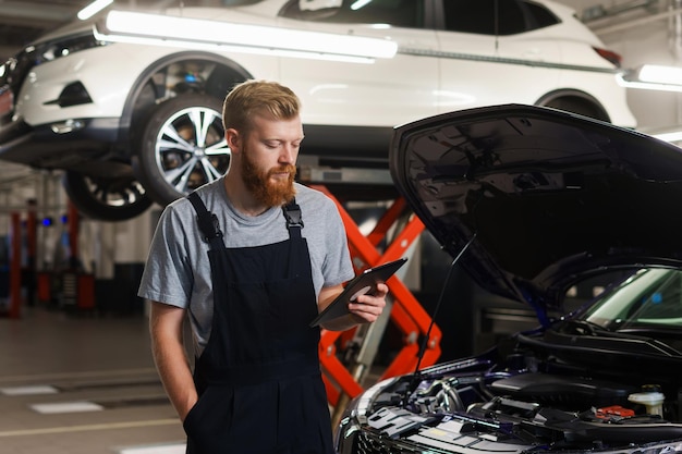 Een mannelijke monteur staat met een tablet en kijkt naar een reparatietoepassing tegen de achtergrond van een professioneel tankstation