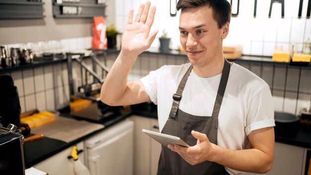 Een mannelijke ober een werknemer in uniform in een café gebruikt een tablet en houdt de kosten bij