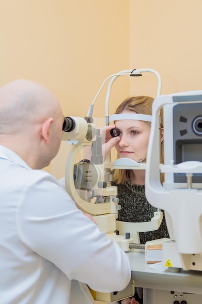 Een mannelijke oogarts controleert het gezichtsvermogen van een jong meisje met behulp van een modern apparaat met een lichtstraal