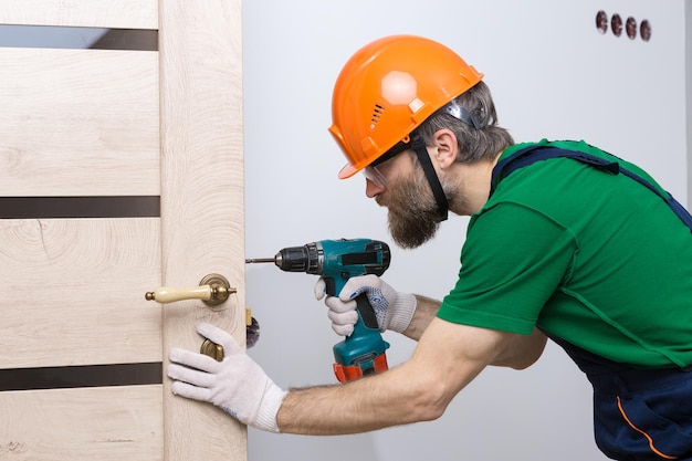 Een mannelijke slotenmaker installeert een deur in een appartement De man werkt met een schroevendraaier