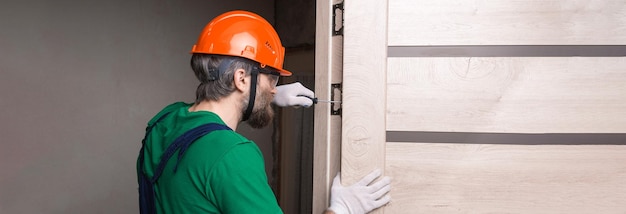 Een mannelijke slotenmaker installeert een deur in een appartement de man werkt met een schroevendraaier
