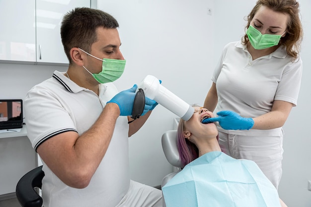 een mannelijke tandarts fotografeert de tanden van een vrouwelijke patiënt naast een vrouwelijke assistent het concept van een tandheelkundige kliniek