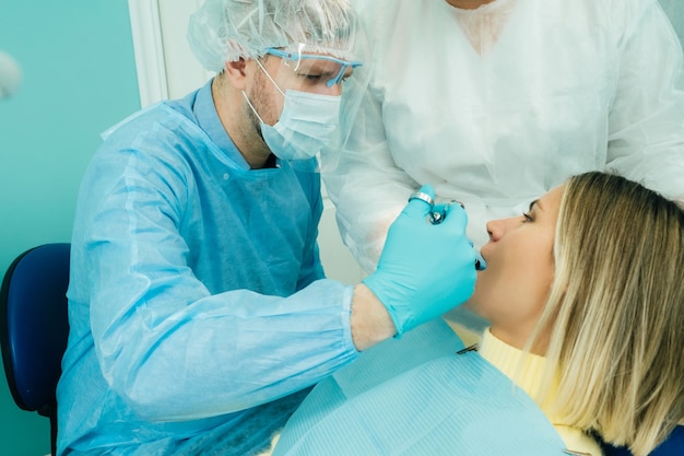 Een mannelijke tandarts met tandheelkundige hulpmiddelen boort de tanden van een patiënt met een assistent. Het concept van medicijnen