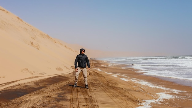 Een mannelijke toerist die een zwarte jas draagt, kijkt naar de oceaan. Sandwich Haven. Namibië.