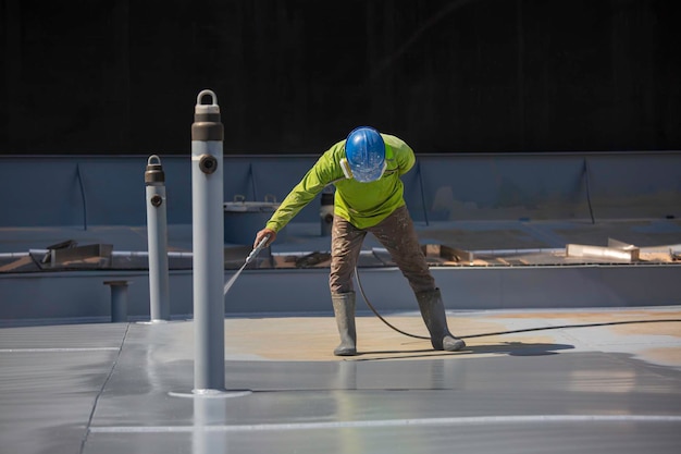 Een mannelijke werknemer die een industrieel spuitpistool vasthoudt dat wordt gebruikt voor het oppervlak van de dakplaattank op stalen industriële verf