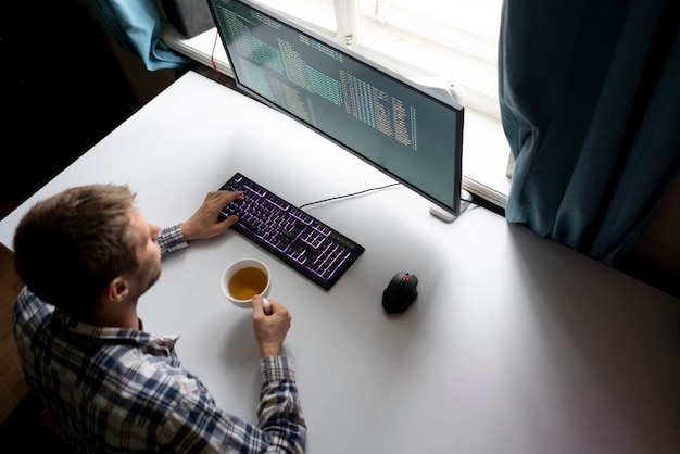 Een mannelijke werknemer op kantoor met een kop warme drank achter de computer