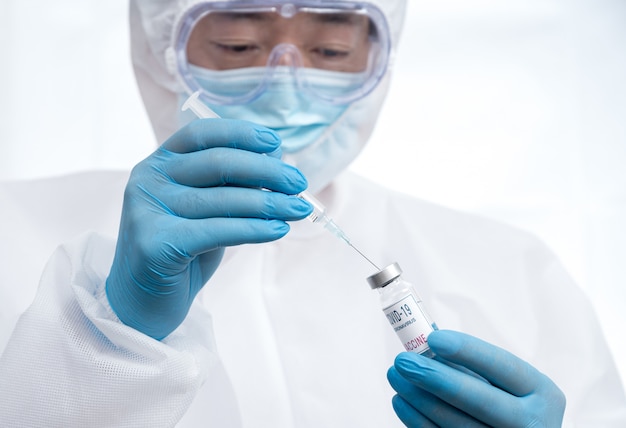 Een mannelijke wetenschapper met blauwe handschoenen en een beschermend pak met een Covid-19-vaccin.