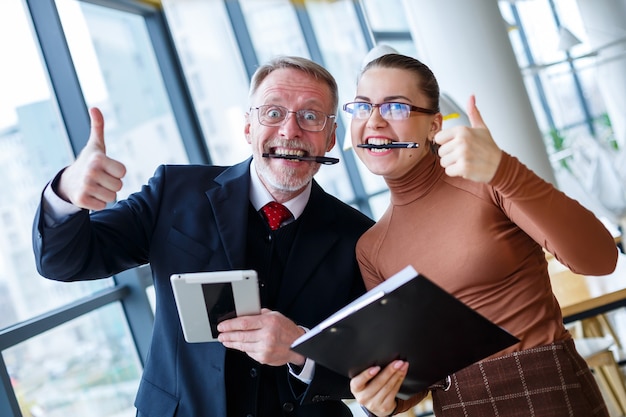 Een mannelijke zakenman en een vrouw ondertekenen een contract en vieren succes in zijn kantoor. Houd pennen tussen hun tanden en glimlach