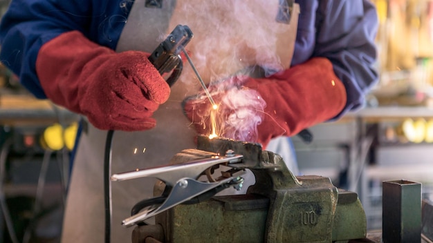 Een mannenlasser met veiligheidshelm die met een booglasmachine in de werkplaats werkt