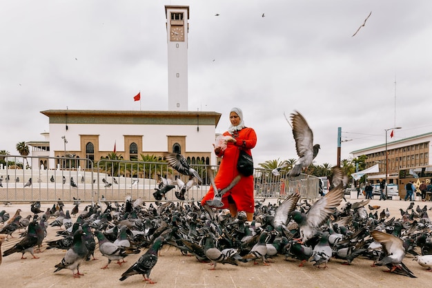 Een Marokkaanse vrouw in een rode jurk voert duiven op een plein in de stad Casablanca. Marokko