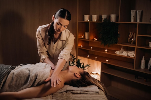 Een masseuse geeft een lichaamsmassage aan een vrouw in een kuuroord Een professionele masseur masseert de schouder van een meisje dat in een kuuroord ligt