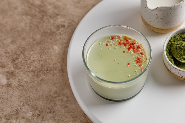 Een matcha thee panna cotta dessert met decor in een glas op een wit dienblad en beige achtergrond