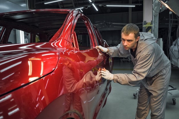 Een medewerker van de spuiterij van een autofabriek controleert de kwaliteit van het te schilderen oppervlak