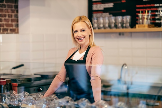 Een medewerker van een pannenkoekenhuis leunt op het aanrecht en glimlacht naar de camera