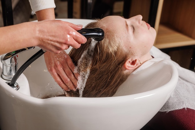 Een meester in een schoonheidssalon wast het haar van een klant met shampoo voor haarverzorging in een schoonheidssalon