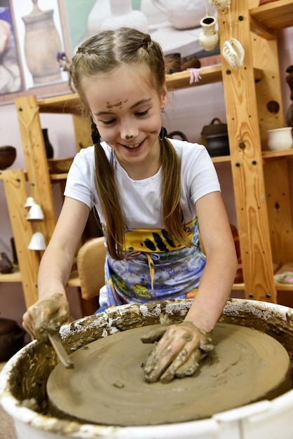 Een meisje beeldhouwt een kan op een pottenbakkersschijf Creation Childhood