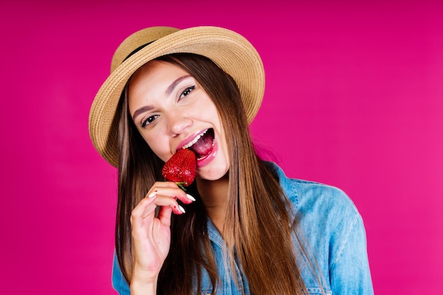 Een meisje dat een aardbei eet op een roze achtergrond