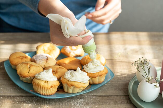 een meisje dat een spuitzak gebruikt, versiert cupcakes met room