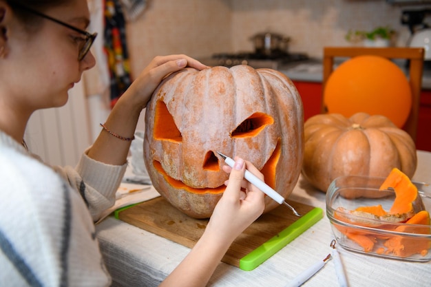 Een meisje dat grote oranje pompoen in jackolantern snijdt voor Halloween-vakantiedecoratie in de keuken Decoratie voor feest