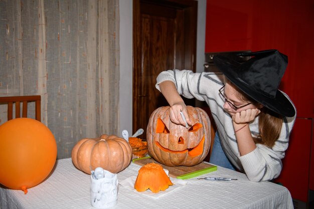 Een meisje dat grote oranje pompoen in jackolantern snijdt voor Halloween-vakantiedecoratie in de keuken Decoratie voor feest