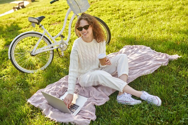 Een meisje dat op het gras in het park zit en op een laptop werkt