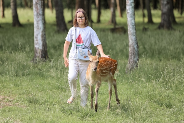 Een meisje dat schattige gevlekte hertenbambi voedt op de kinderboerderij. Gelukkig reizigersmeisje geniet van het socialiseren met wilde dieren in het nationaal park in de zomer. Baby fawn herten spelen met mensen in contact dierentuin