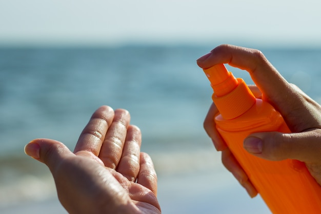 Een meisje die een fles zonnescherm houden en zonnescherm op de palm op tropische strandvakantie toepassen