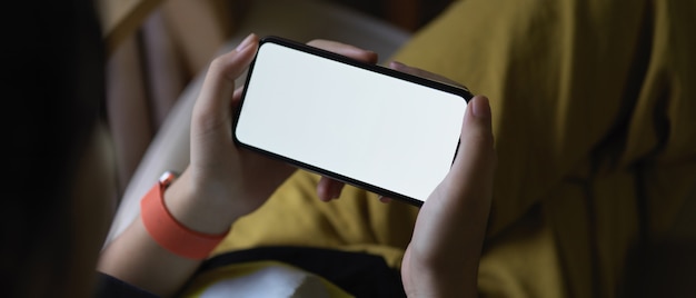 Foto een meisje die horizontale smartphone houden terwijl het zitten met haar benen kruiste op leunstoel in woonkamer