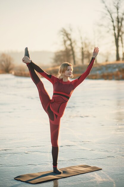 Een meisje doet yoga in de winter op het ijs van het meer tijdens de zonsondergang