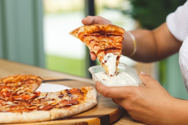 Een meisje doopt een stuk pizza in saus in een plastic bakje voordat ze het eet