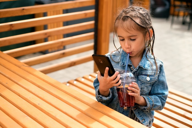 Een meisje drinkt een limonade en kijkt naar haar mobiele telefoon