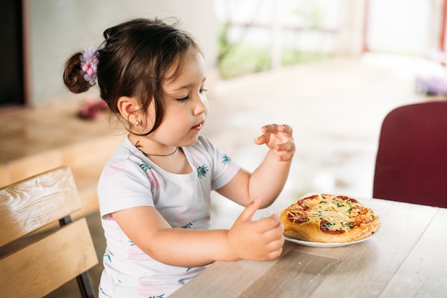 Een meisje, een kind op straat eet een minipizza erg smakelijk