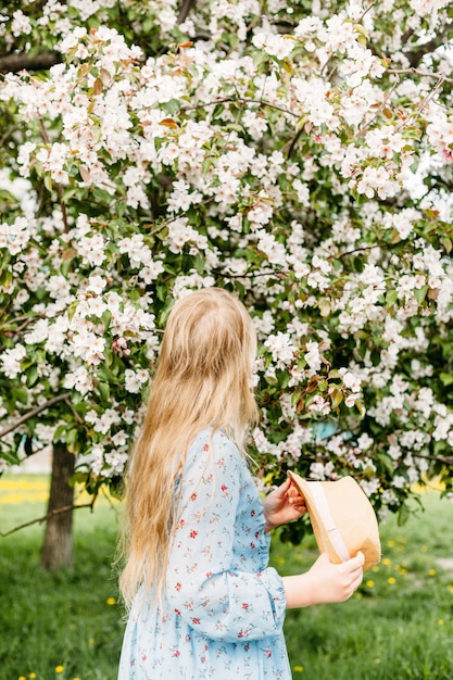 Foto een meisje, een tiener met een hoed loopt in de lente in de stad, bloeiende bomen, een appelboom, het gezicht is niet zichtbaar