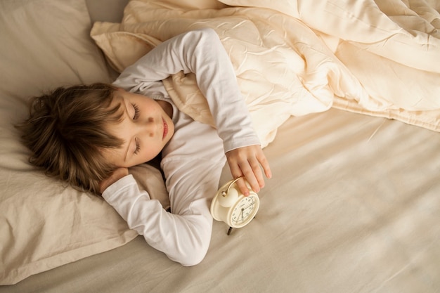 Een meisje een vrouwelijk kind ligt rustig in een bed met een wekker in haar handen, de zon schijnt door het raam