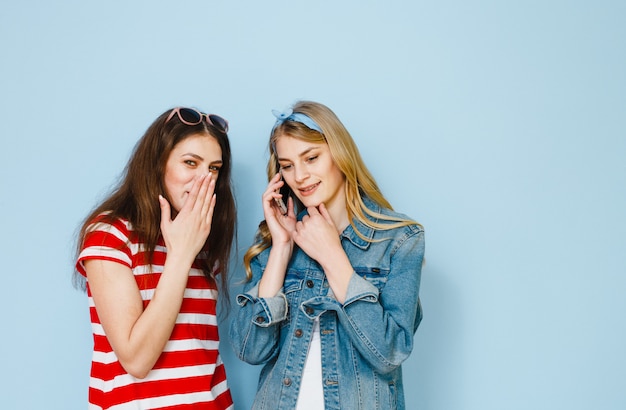 Een meisje fluistert iets in het oor van haar vriendin door naar haar mobiele telefoon te kijken