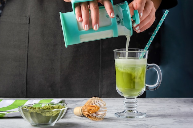 Een meisje giet melk in een glas met matcha groene thee. Het proces om gezonde latte te maken. Bijgesneden foto