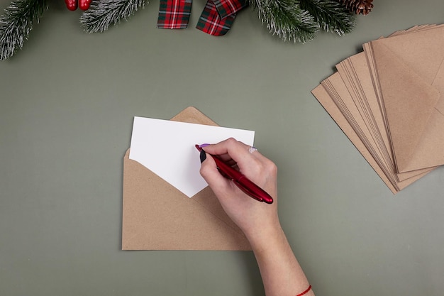 Een meisje houdt een balpen boven een blanco wit vel in een ambachtelijke envelop. Mockup van uitnodiging en wenskaart.