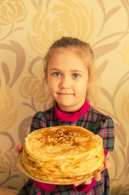 Een meisje houdt een bord met een stapel pannenkoeken vast