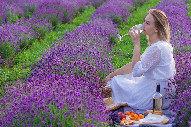 Een meisje houdt een glas witte wijn vast tegen de achtergrond van een lavendelveld Een meisje drinkt wijn in een lavendelveld