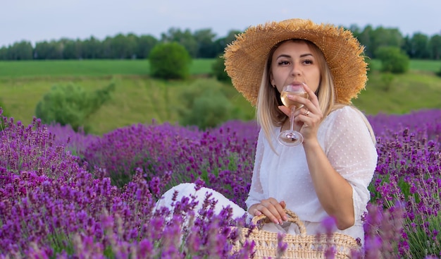 Een meisje houdt een glas witte wijn vast tegen de achtergrond van een lavendelveld Een meisje drinkt wijn in een lavendelveld